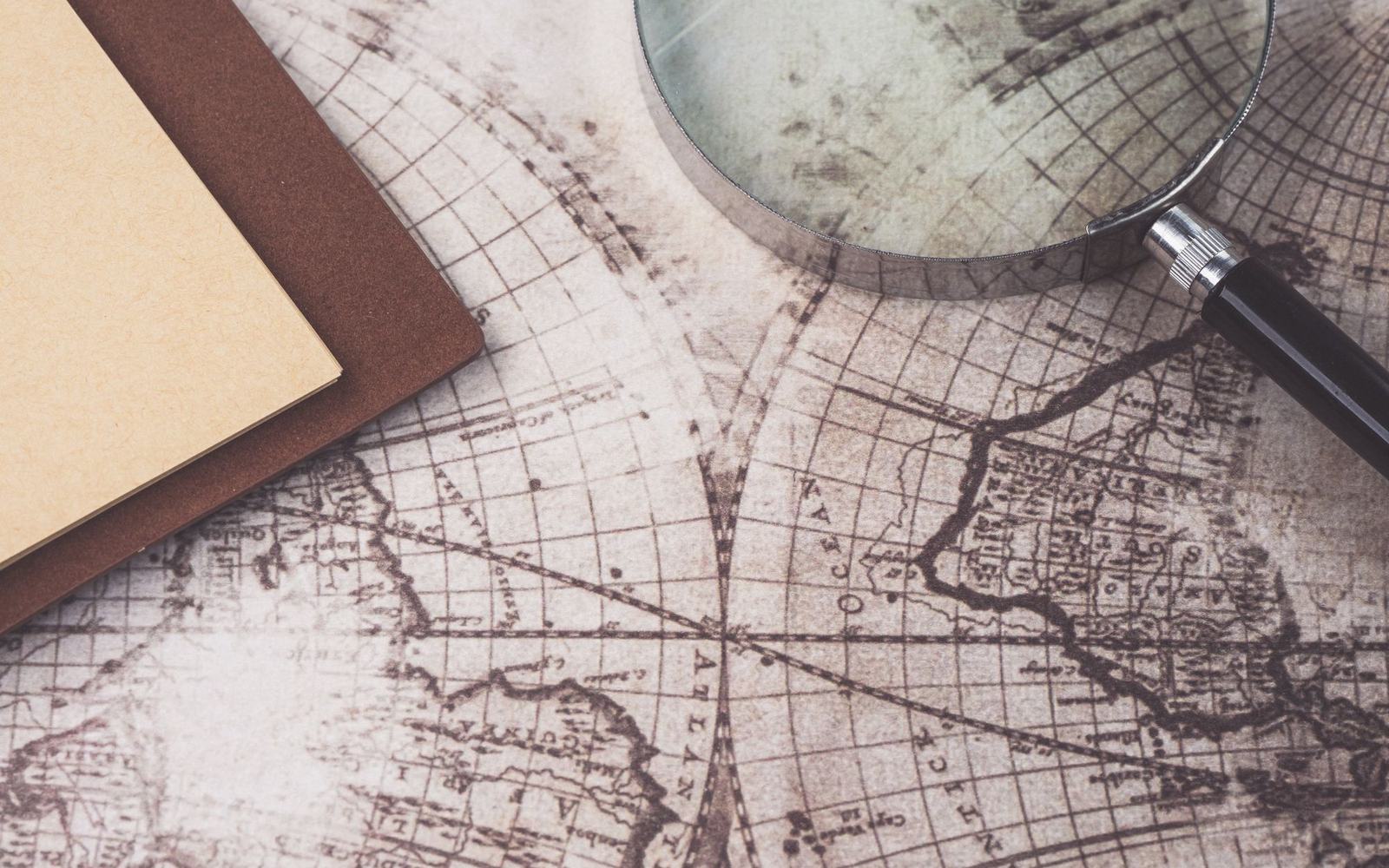 A magnifying glass and notebook resting on an antique world map